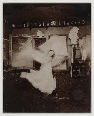 Loïe Fuller practicing at home in front of a Mucha playbill, Passy near Paris